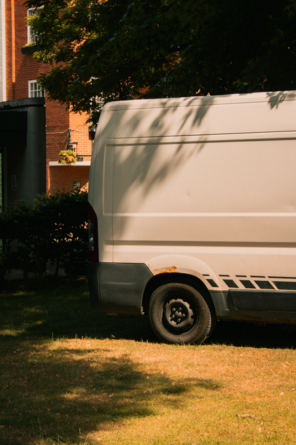 A young man with dark, curly hair wearing a white shirt with red and purple horizontal stripes is seated at a desk, working intently on a keyboard connected to a computer monitor displaying lines of c
