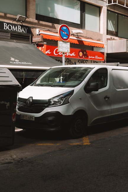 A white van is parked on the street outside a shop on Beckenham High Street, close to a no-parking traffic sign mounted on a pole. The van’s front door is visible, with the driver's window slightly aj
